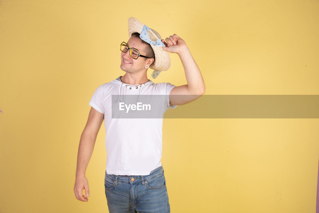 Smiling young man wearing hat standing against yellow background