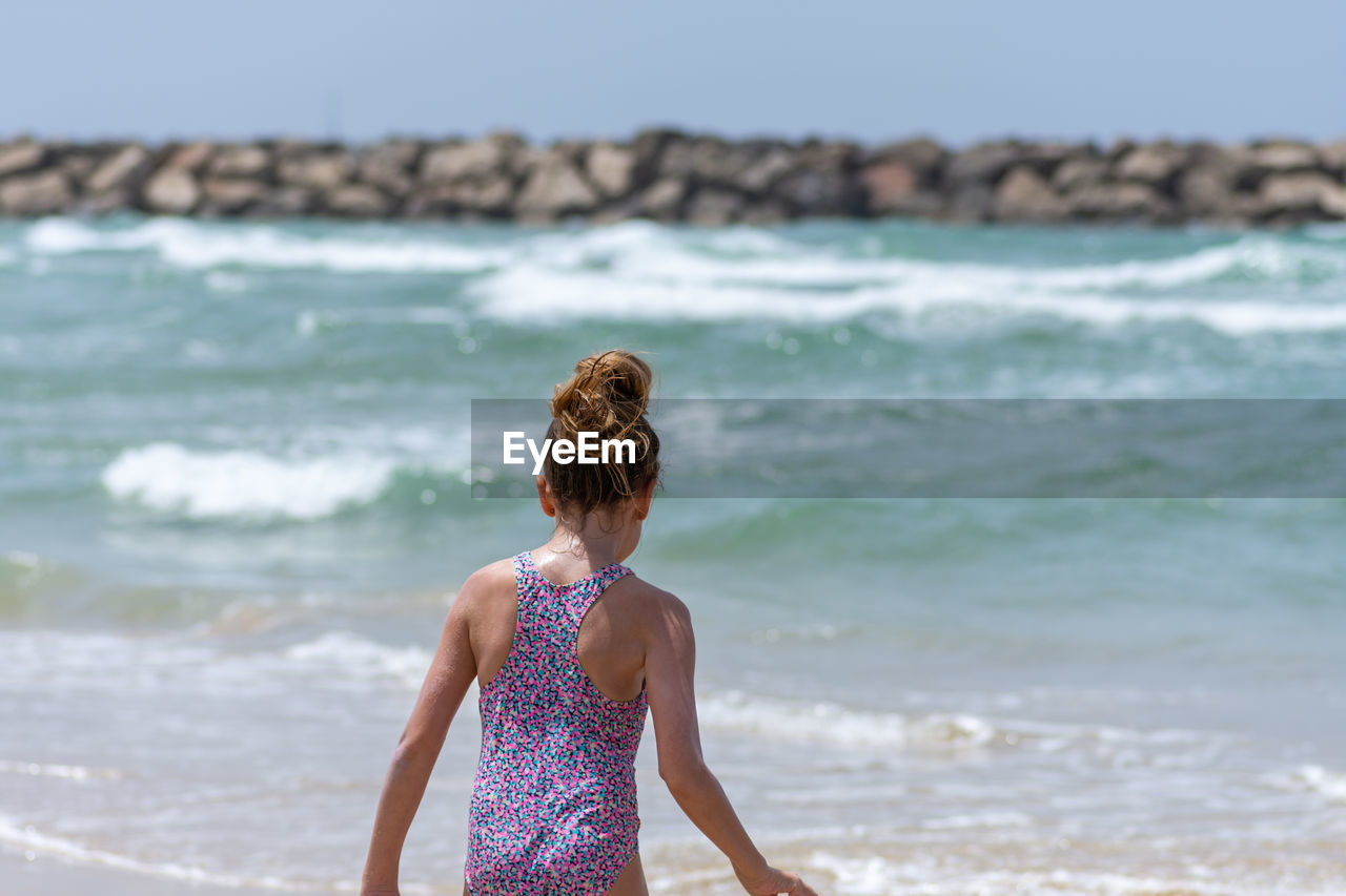 Rear view of girl standing at beach during summer