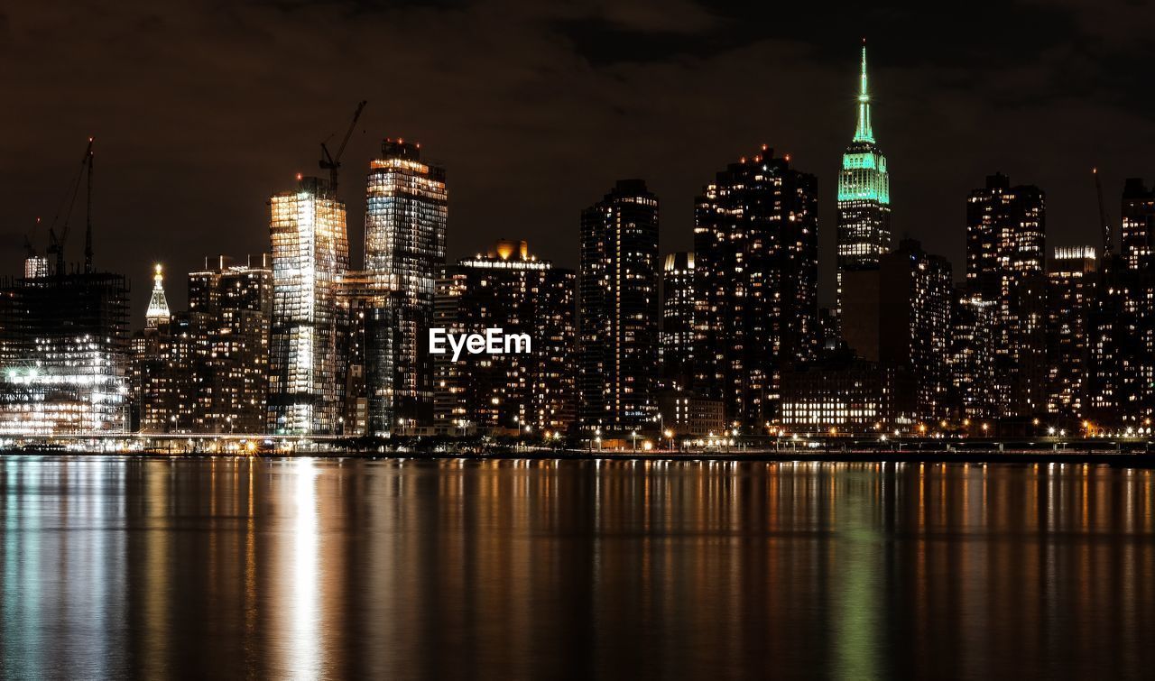 Illuminated empire state building by east river against sky in manhattan at night