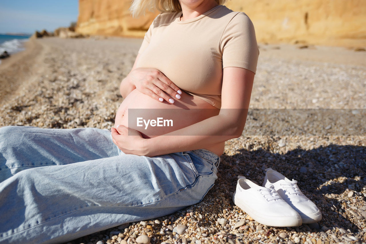 MIDSECTION OF WOMAN SITTING ON SHORE