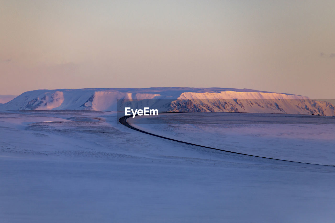 Empty winding asphalt roadway leading through valley covered with snow in highlands during sunset in winter in iceland