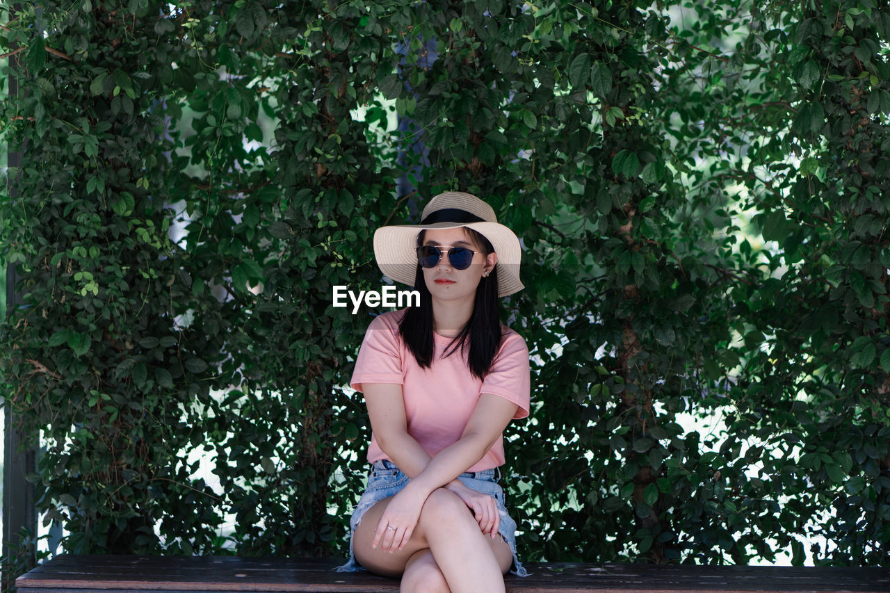 Portrait of young woman wearing hat sitting against plants