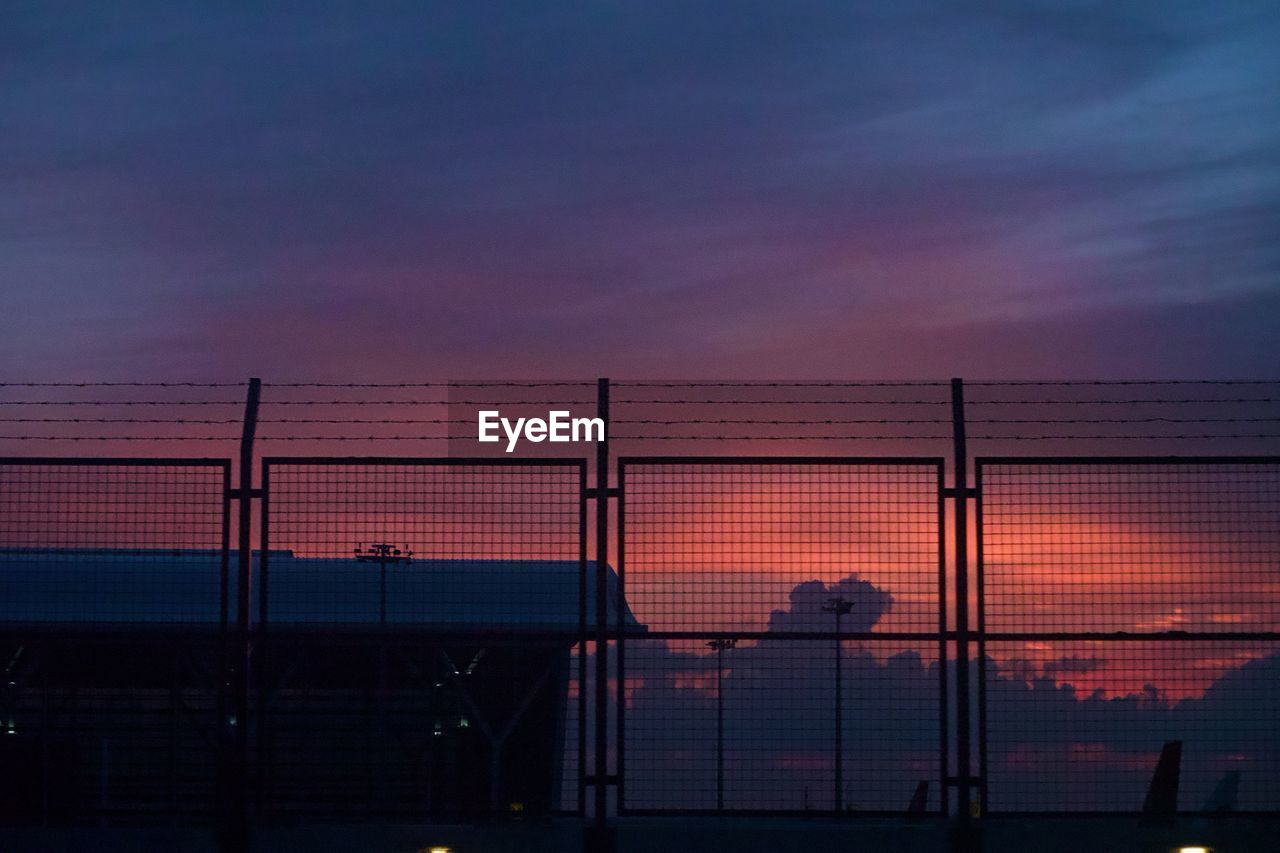 Silhouette fence against orange sky