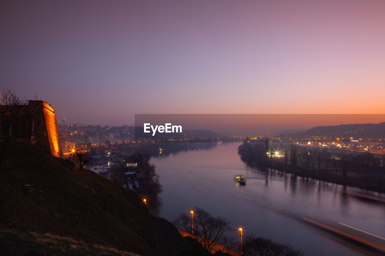 HIGH ANGLE VIEW OF ILLUMINATED BUILDINGS BY RIVER AGAINST SKY