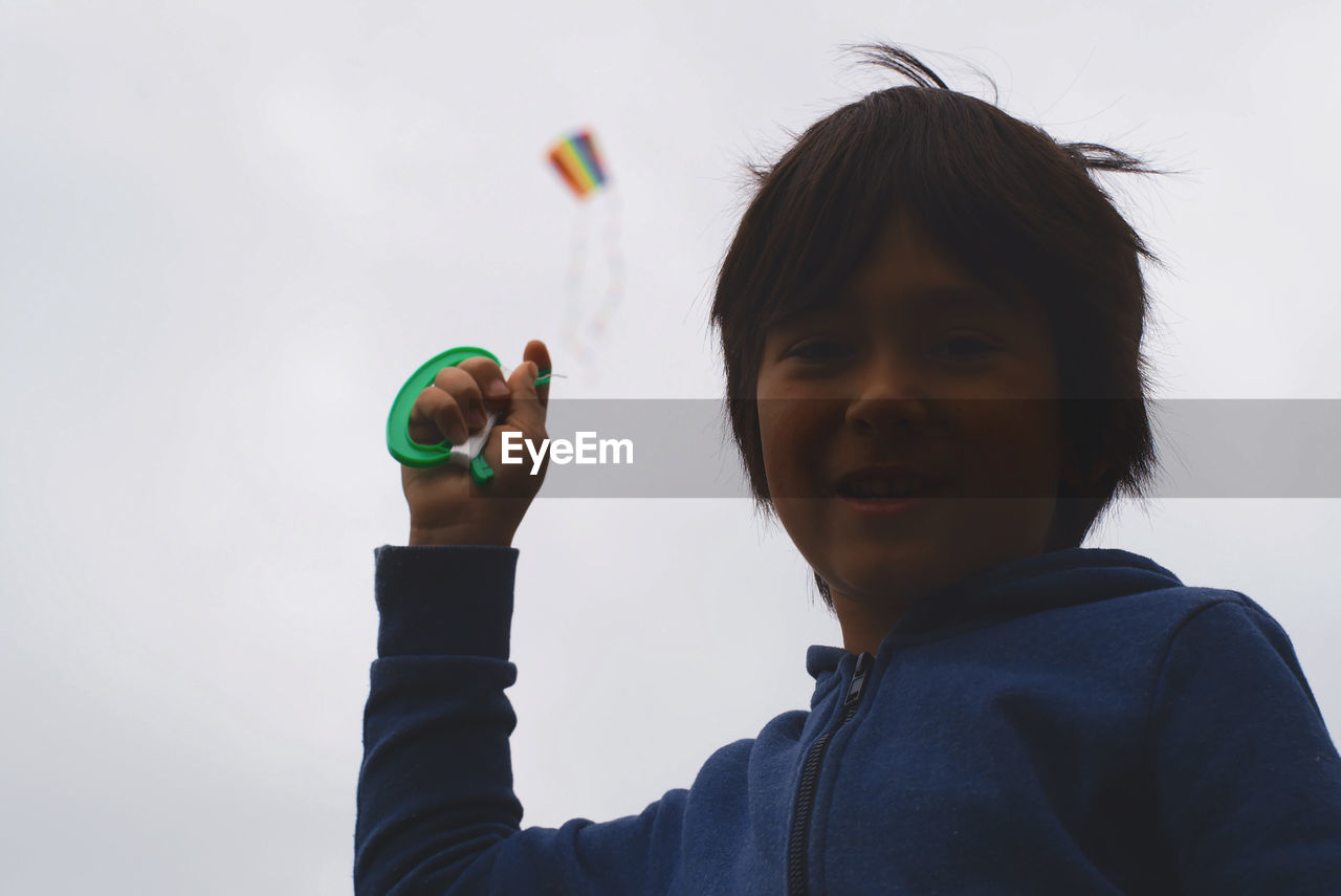 Low angle portrait of boy flying kite in sky
