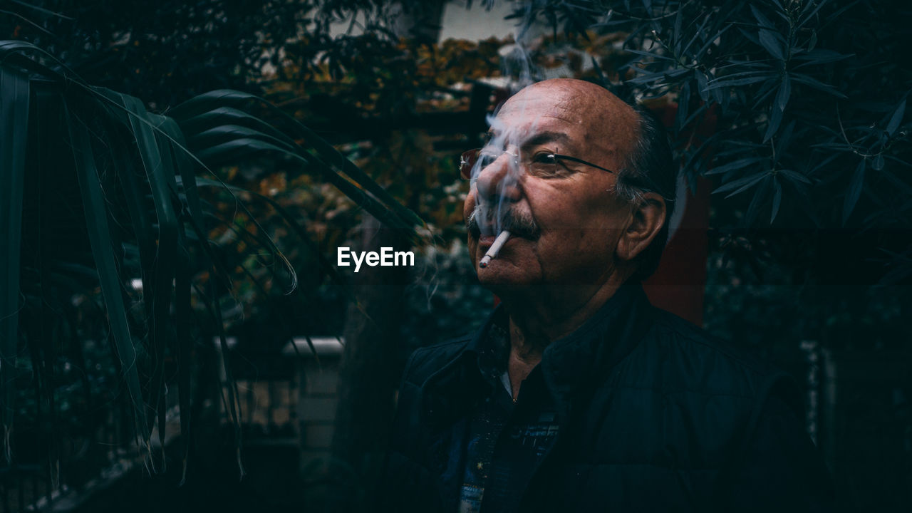 Man smoking cigarette against trees