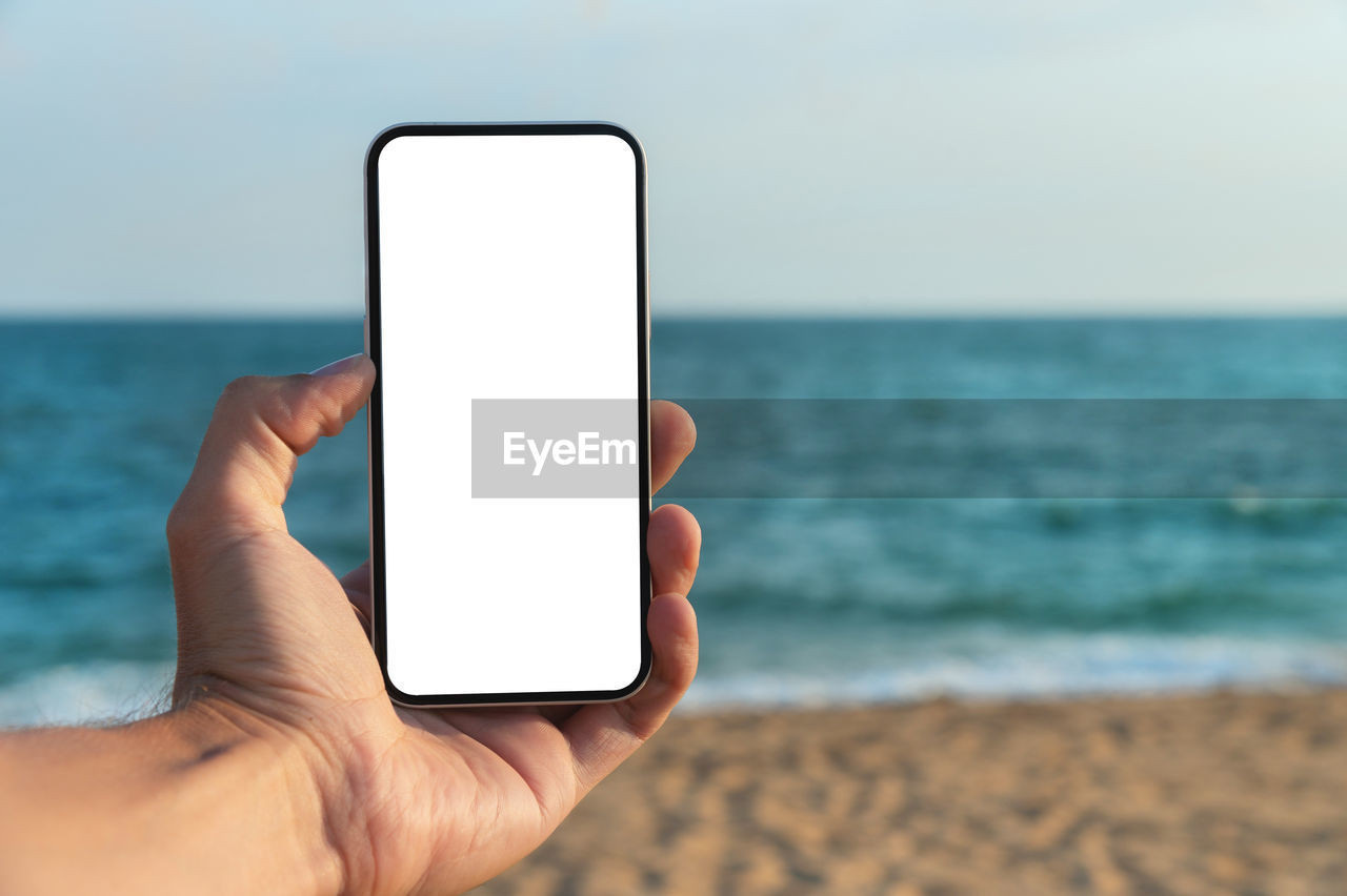 Hand holding smartphone on the beach, mobile mockup of blank screen, take your screen to put on