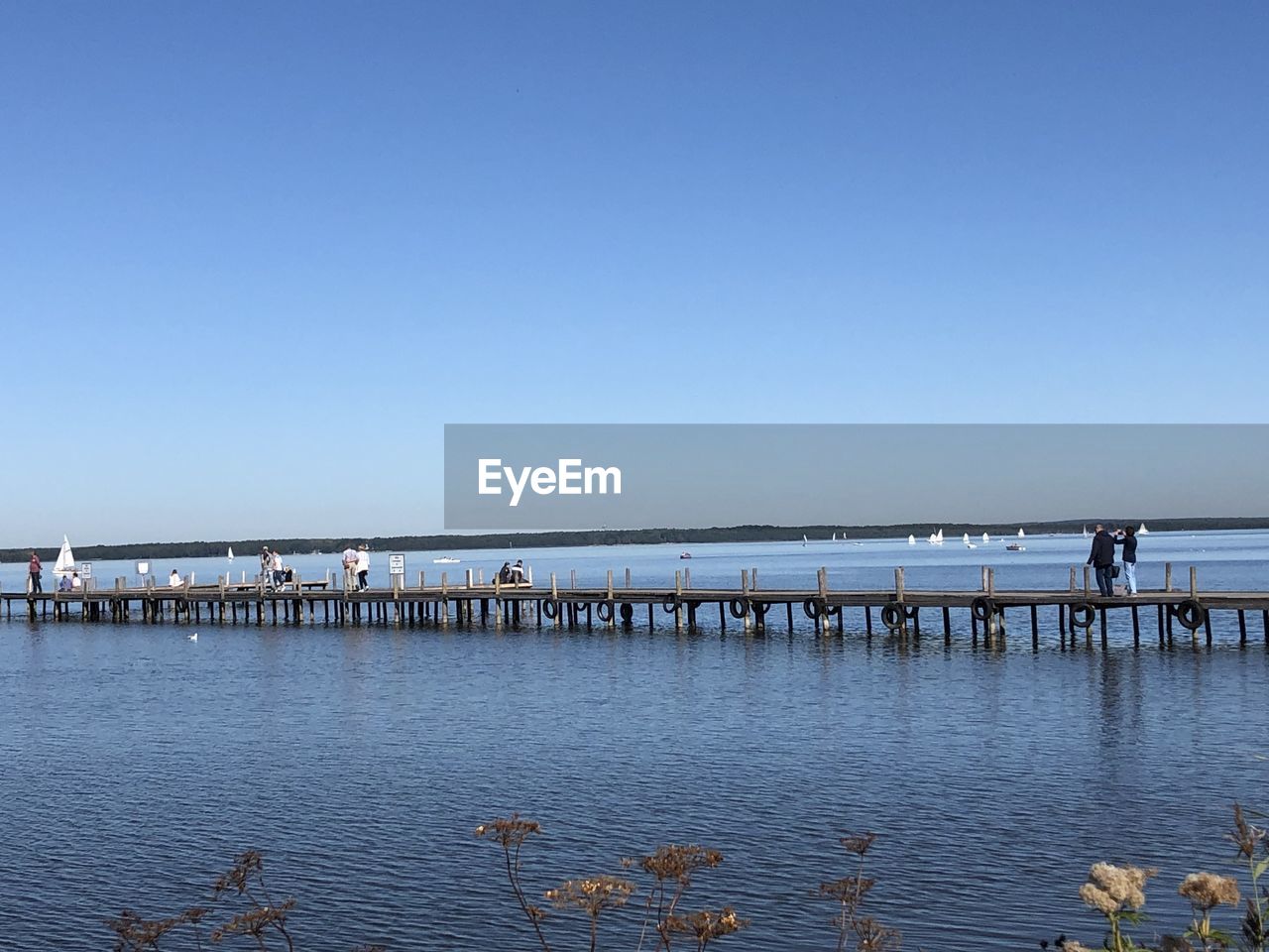 People on pier over sea against clear blue sky