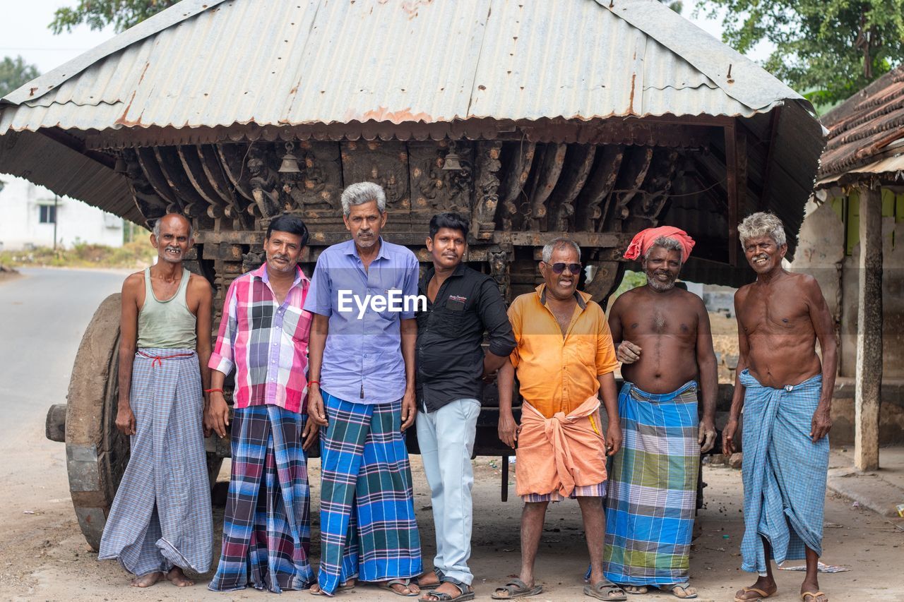group of people, men, adult, traditional clothing, hut, tourism, village, architecture, tribe, tradition, full length, clothing, portrait, women, indigenous culture, nature, female, senior adult, day, building exterior, smiling, standing, togetherness, outdoors, person, child, childhood, built structure, happiness, group, rural scene, mature adult, roof, travel, looking at camera