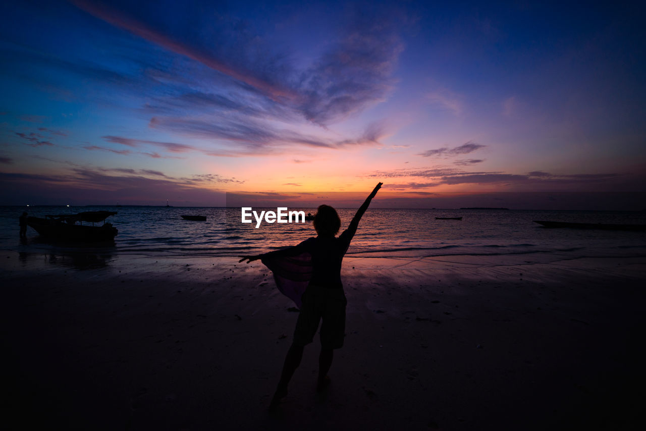 SILHOUETTE MAN STANDING ON BEACH DURING SUNSET