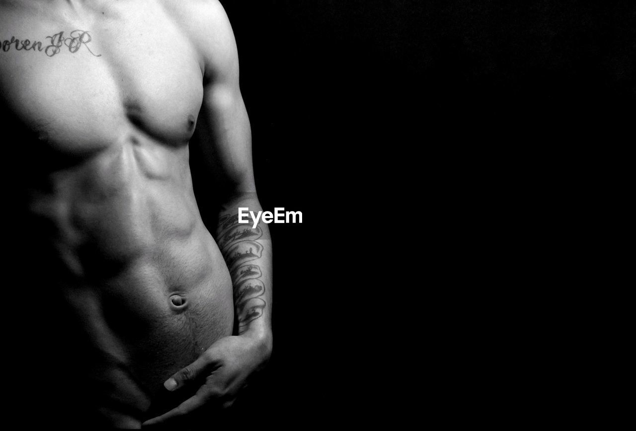 Midsection of shirtless muscular man against black background