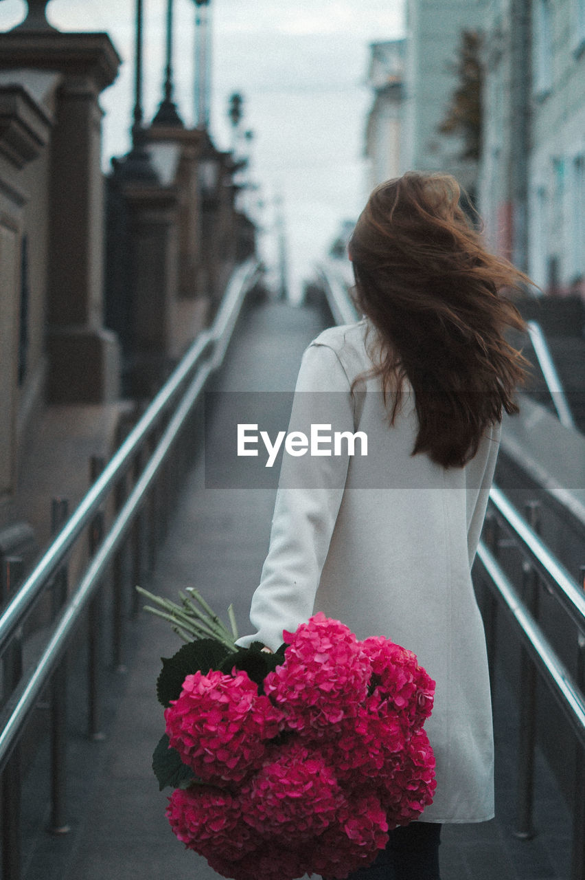 Rear view of woman with pink flowers walking in alley