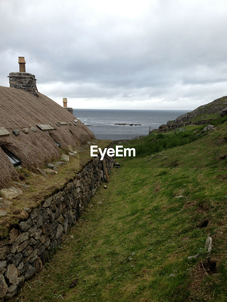 Hut on hill by sea against cloudy sky