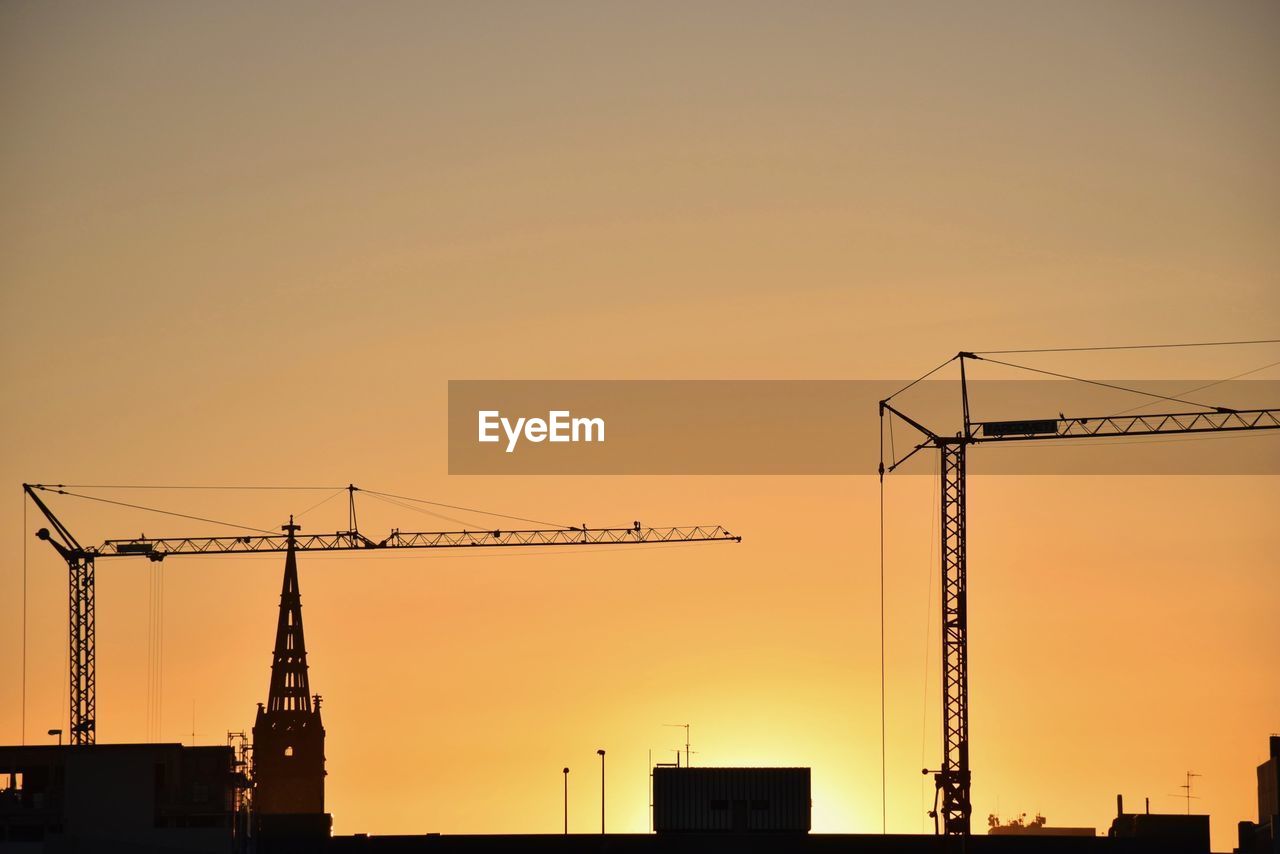 Low angle view of silhouette cranes against orange sky