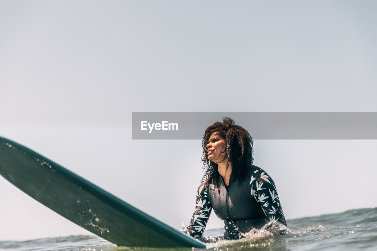 Black woman sitting on her surfboard in the water