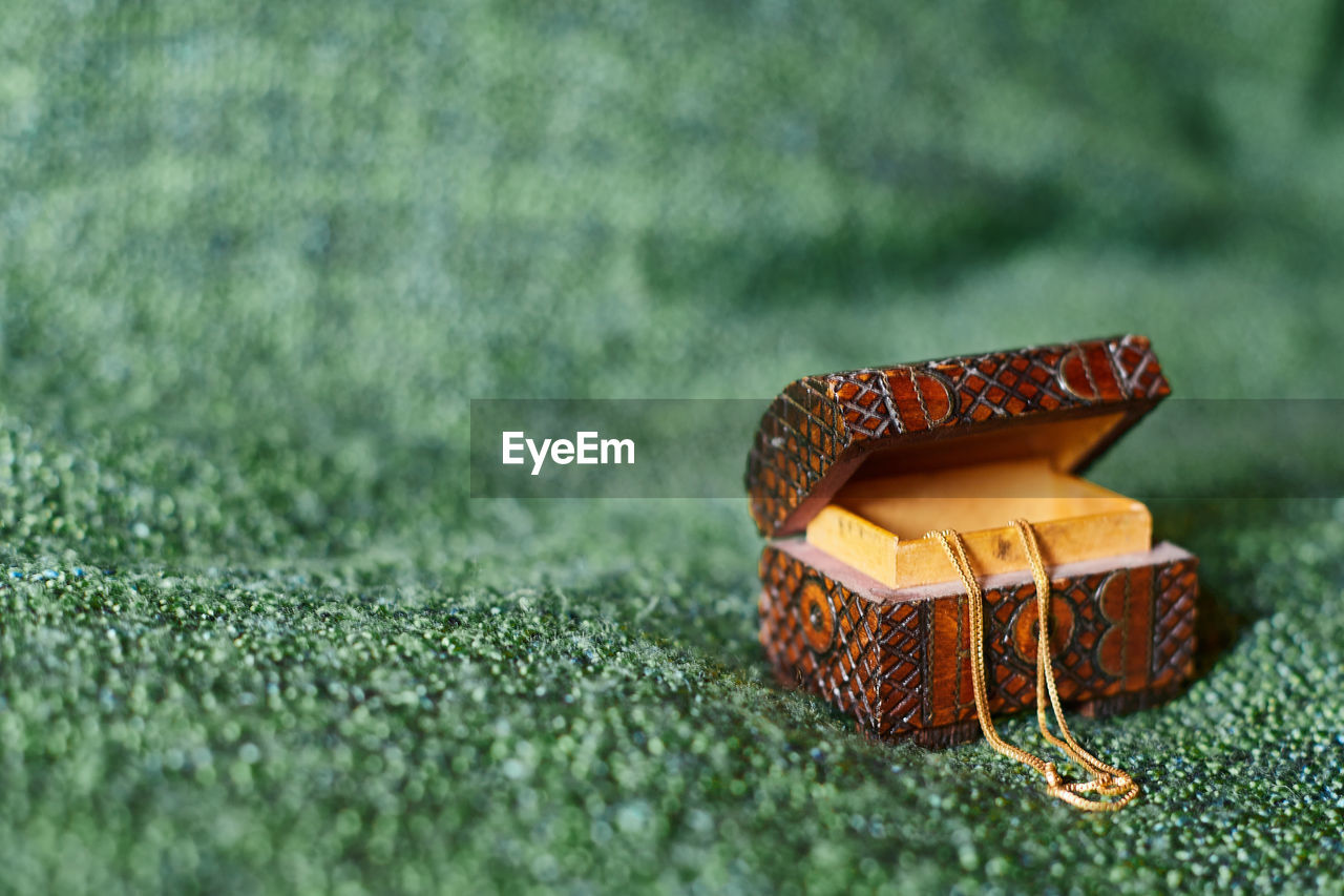 A tiny ornamented wooden jewelry box on green background, with a golden chain hanging, offcenter