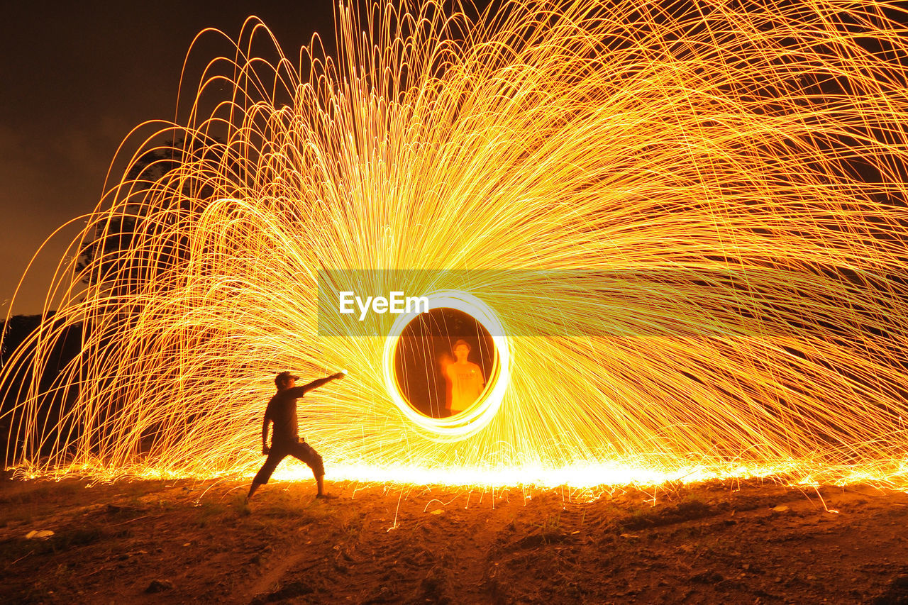 Men standing by spinning wire wool on field at night