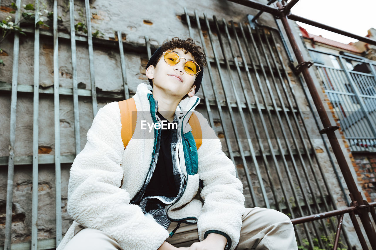 Portrait of boy wearing sunglasses sitting on railing against wall