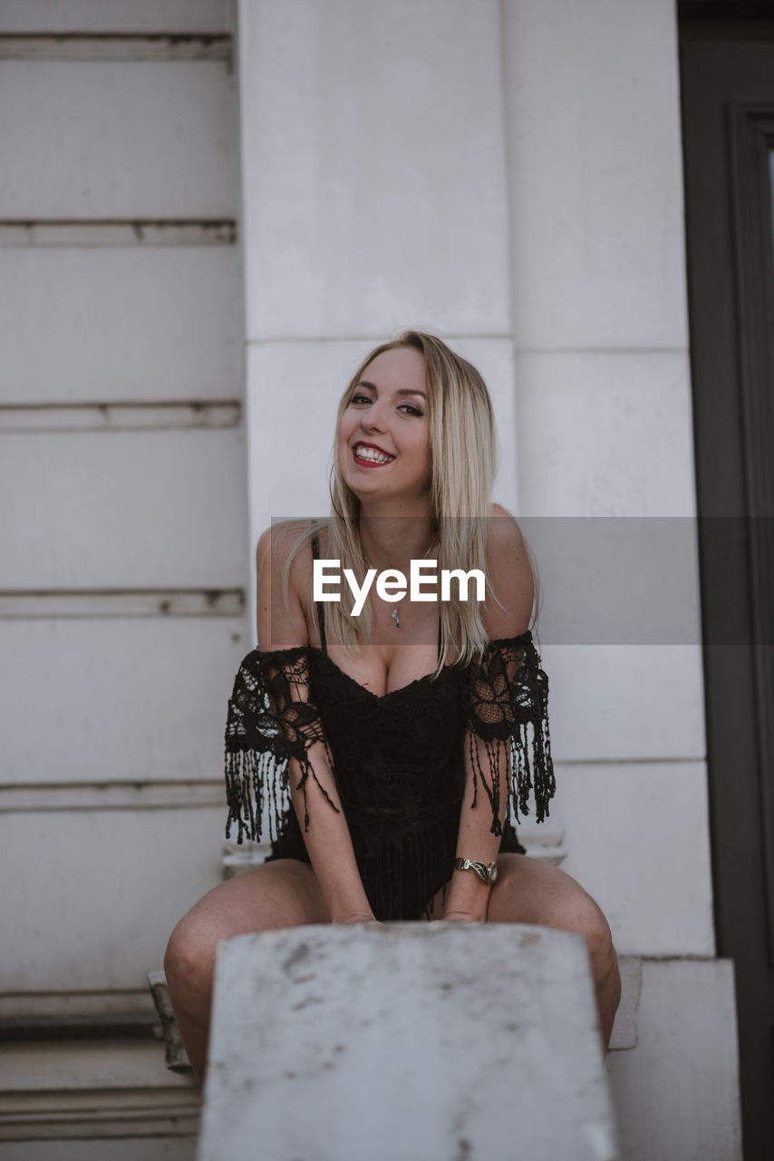 Portrait of beautiful young woman sitting against wall