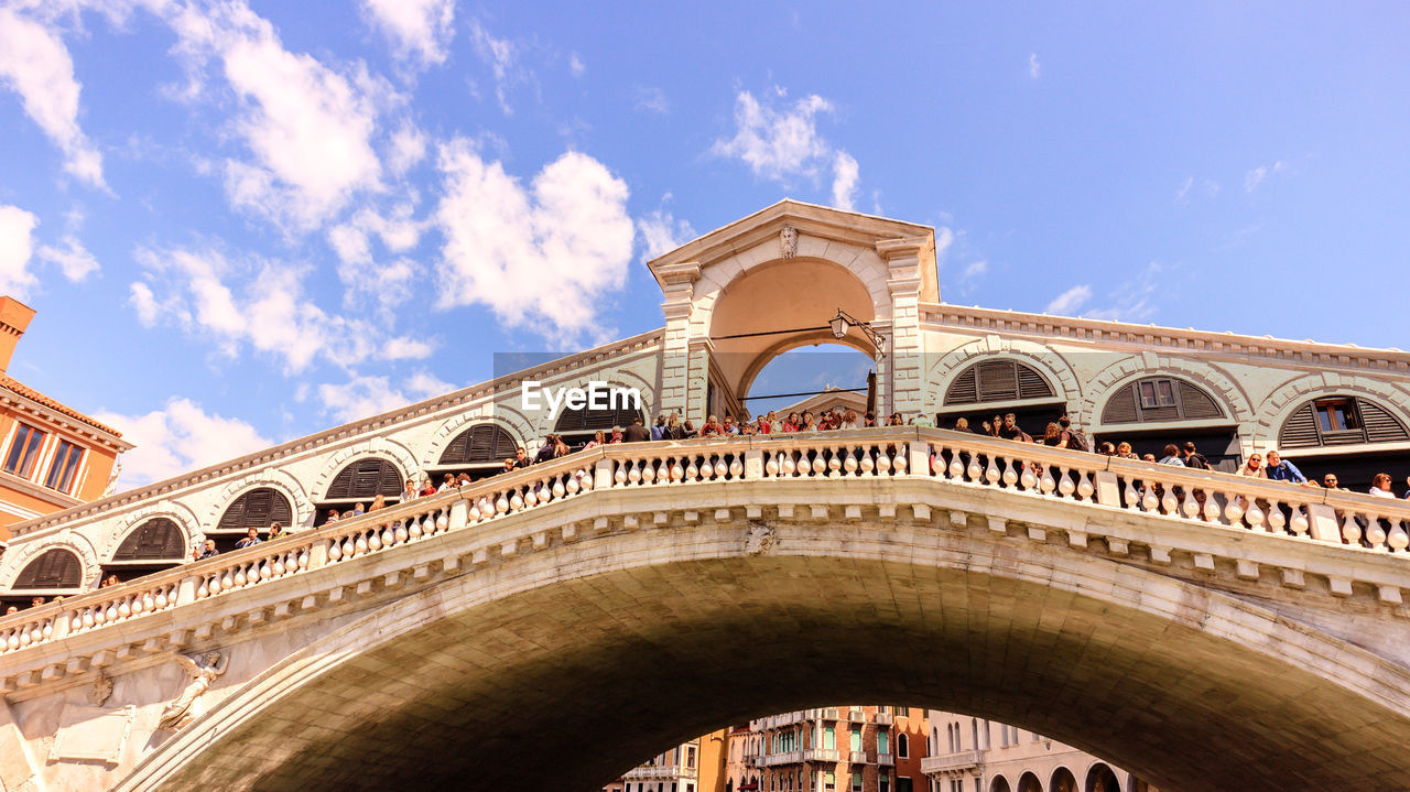 Low angle view of people on arch bridge against sky