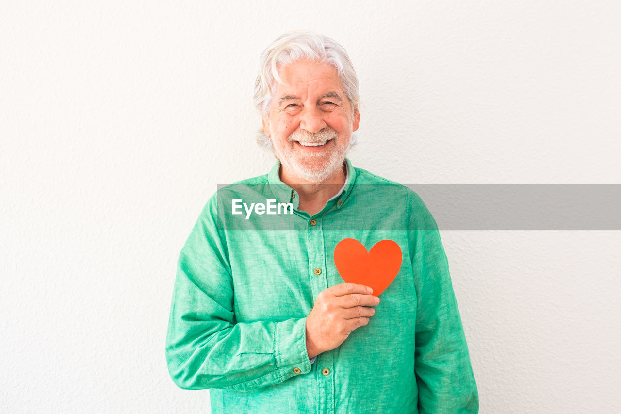 PORTRAIT OF SMILING YOUNG MAN HOLDING HEART SHAPE OVER WHITE BACKGROUND