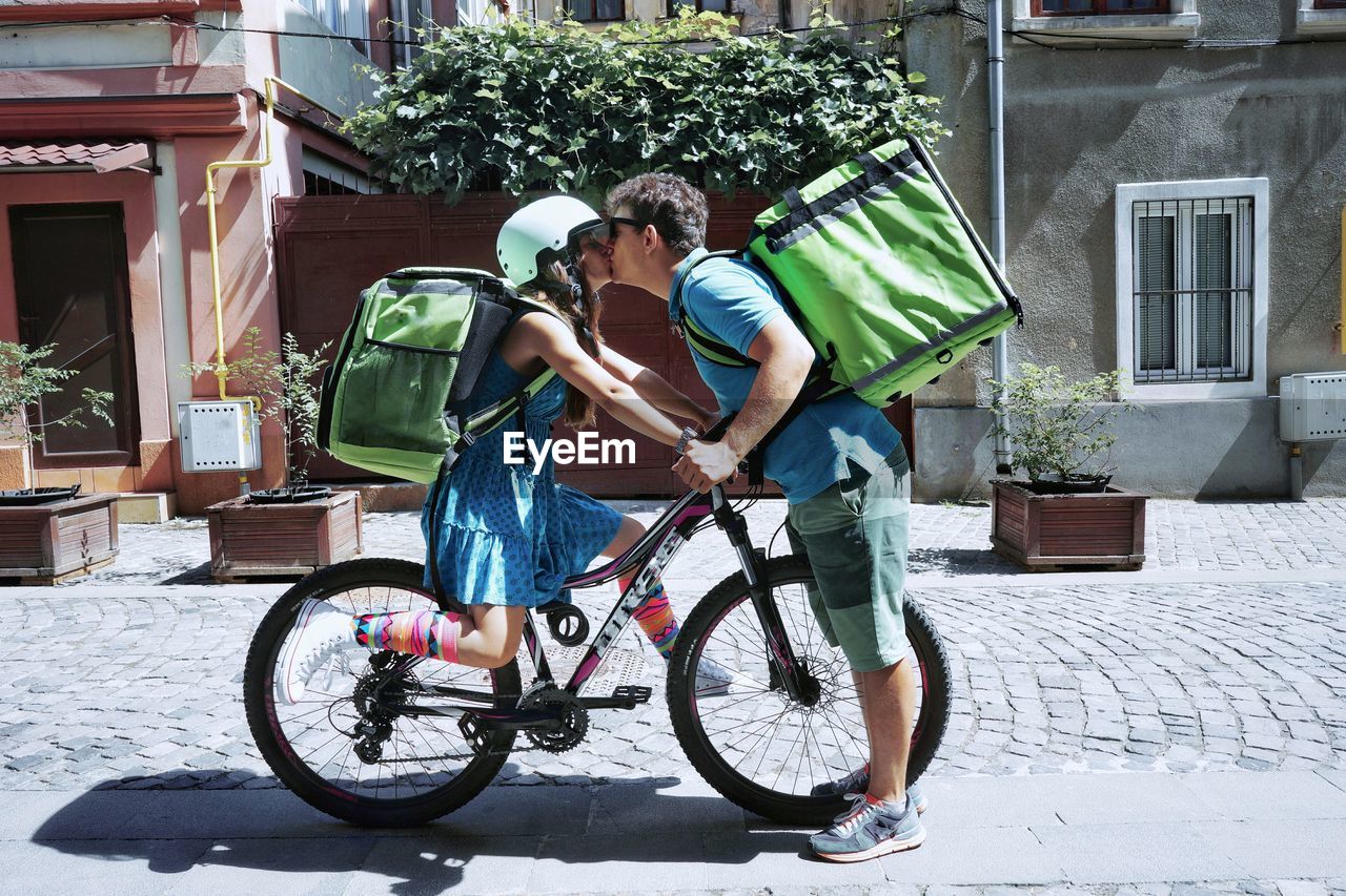 Couple with bicycle kissing on street in city