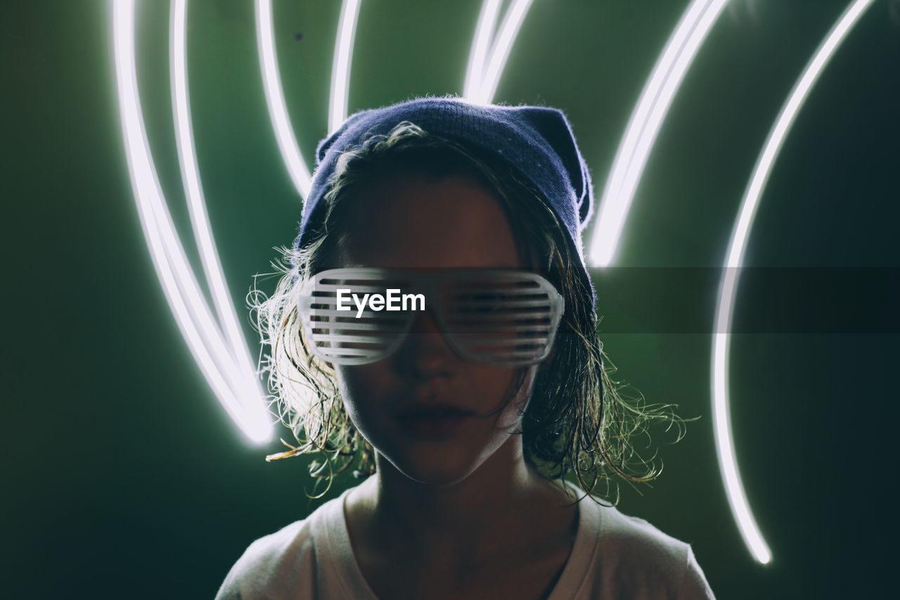 Portrait of girl wearing novelty glasses with light painting against green background