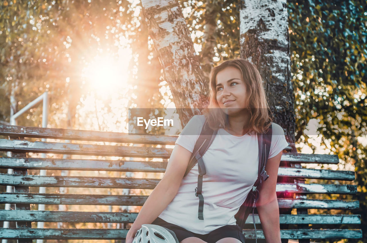 Cheerful pretty girl resting on bench against the background of sun