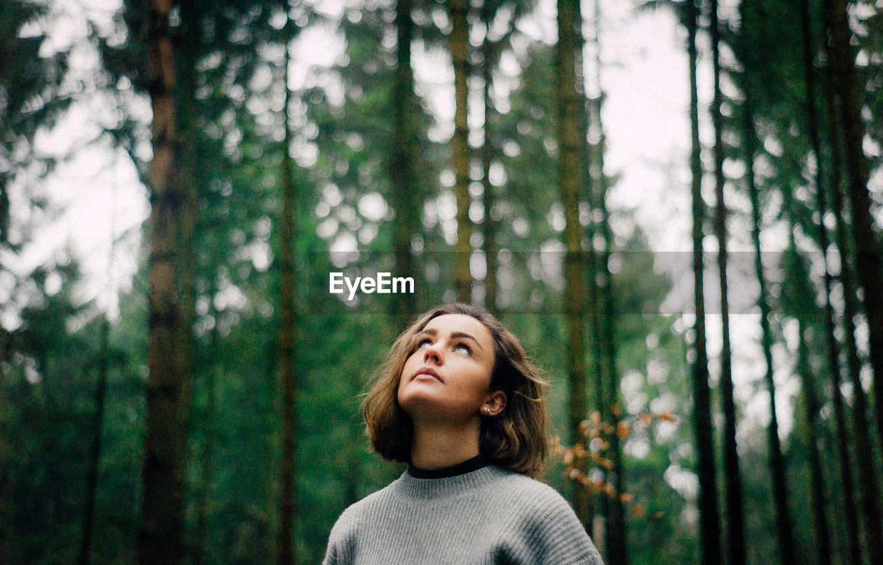 Young woman looking up while standing in forest