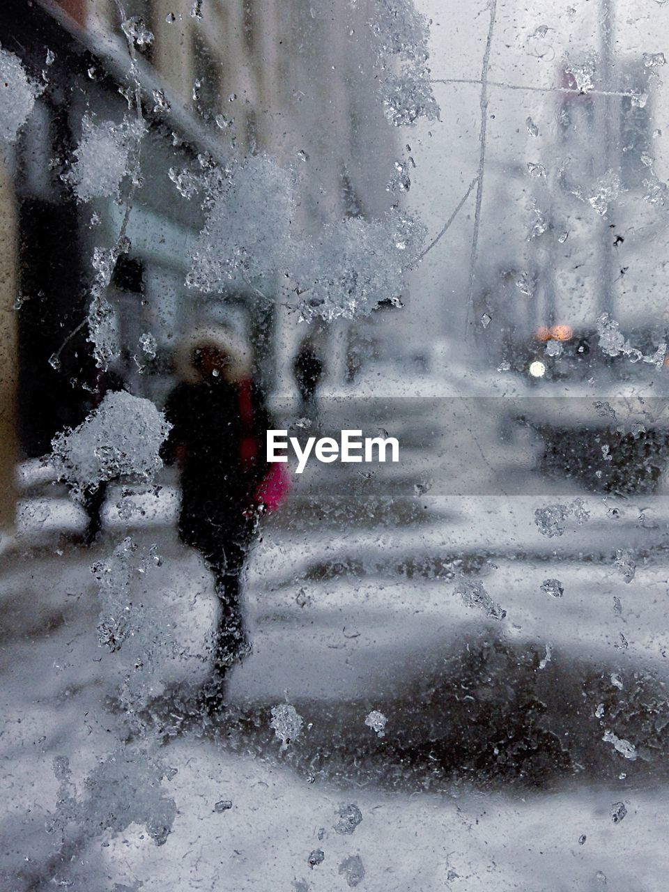 Woman walking on snow covered sidewalk in city seen through window