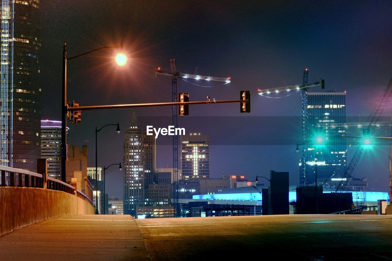 Illuminated street amidst buildings against sky at night