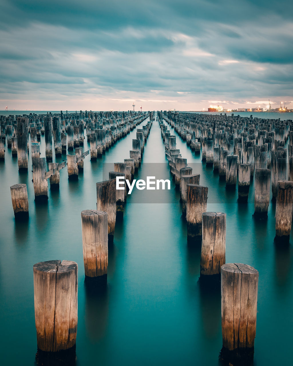 High angle view of wooden posts in sea against cloudy sky during sunset