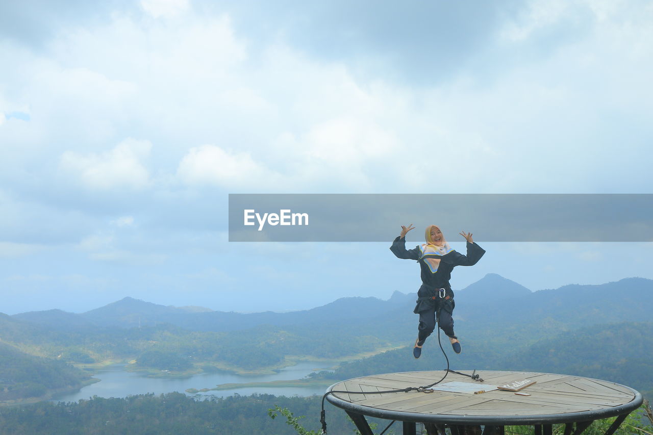 Portrait of smiling woman jumping on built structure against sky