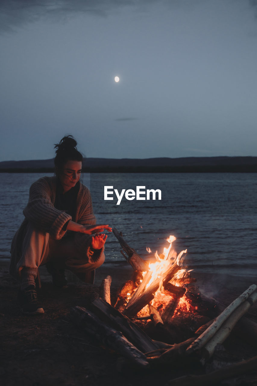 Woman sitting by campfire on beach