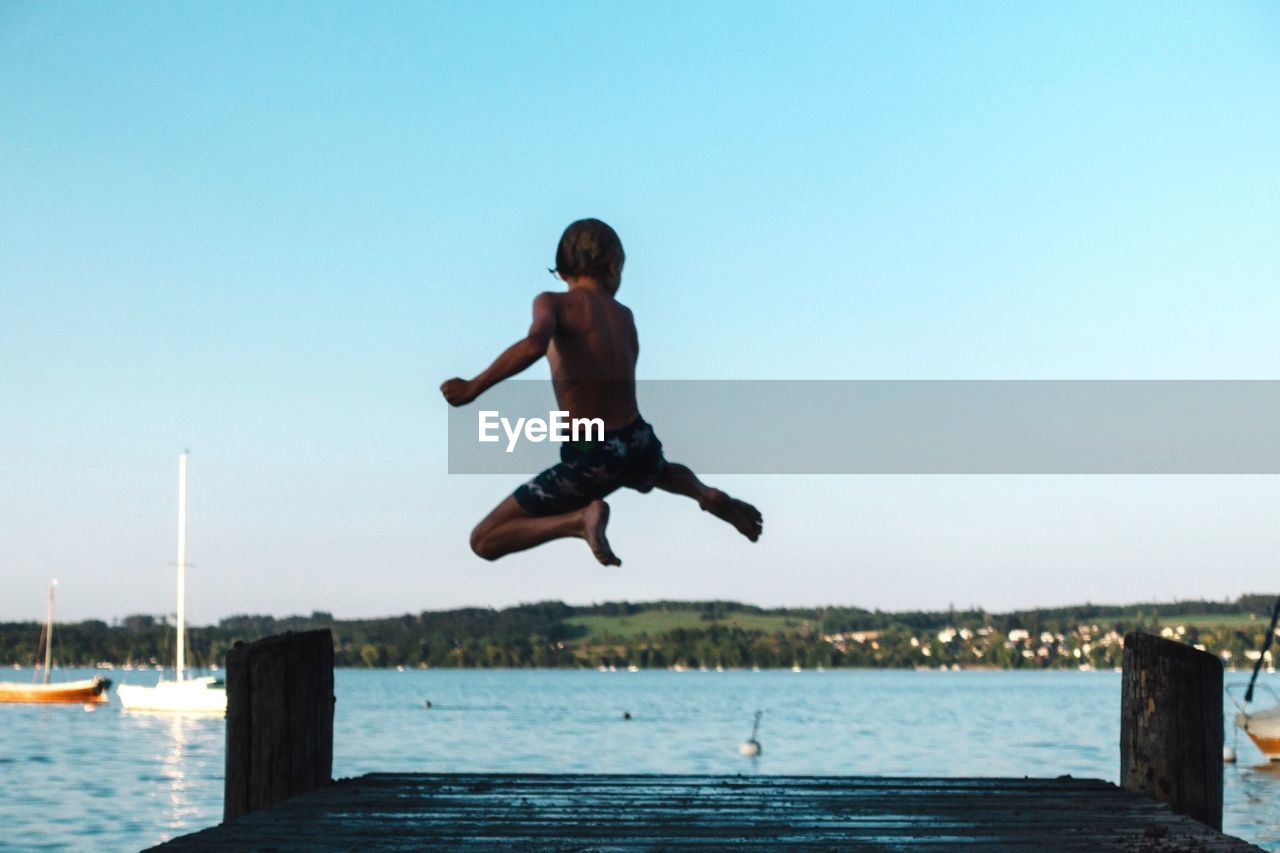 FULL LENGTH OF MAN JUMPING IN SWIMMING POOL AGAINST SKY