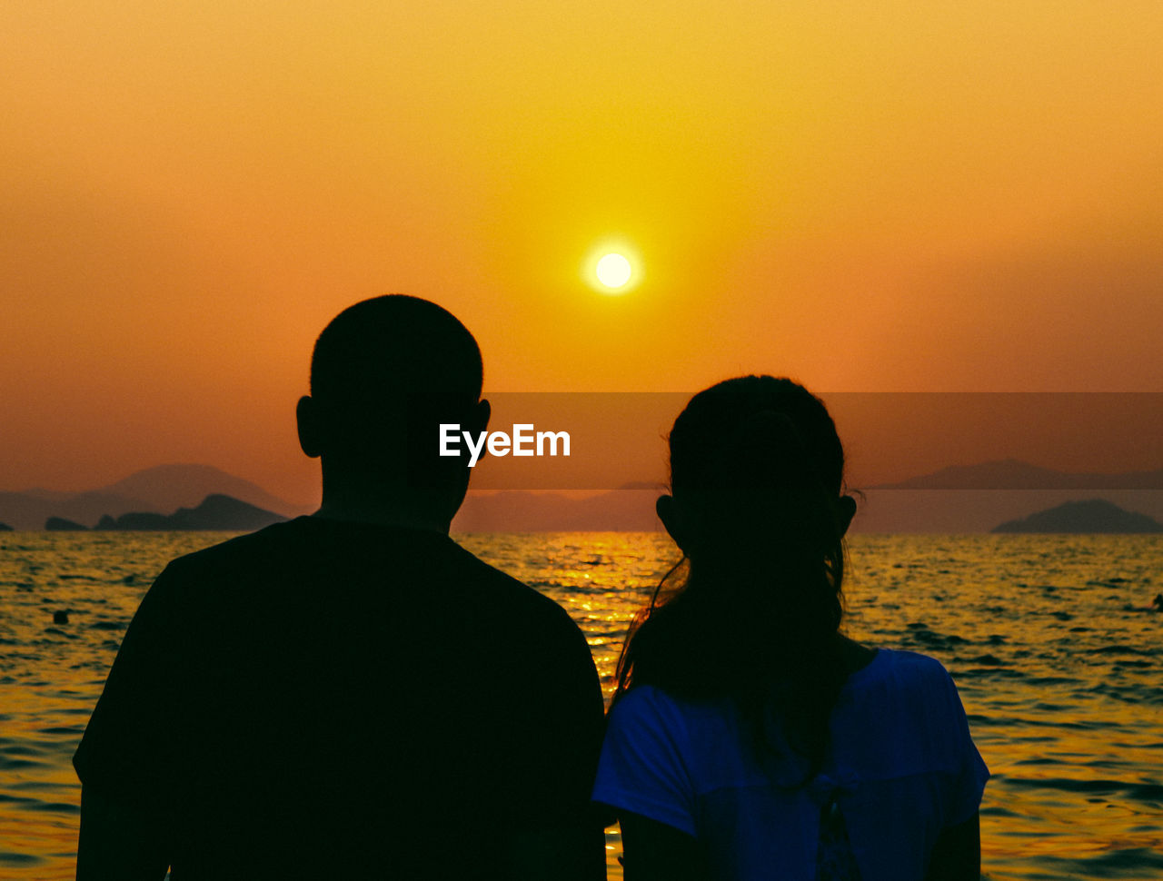 Rear view of people on sea against sky during sunset