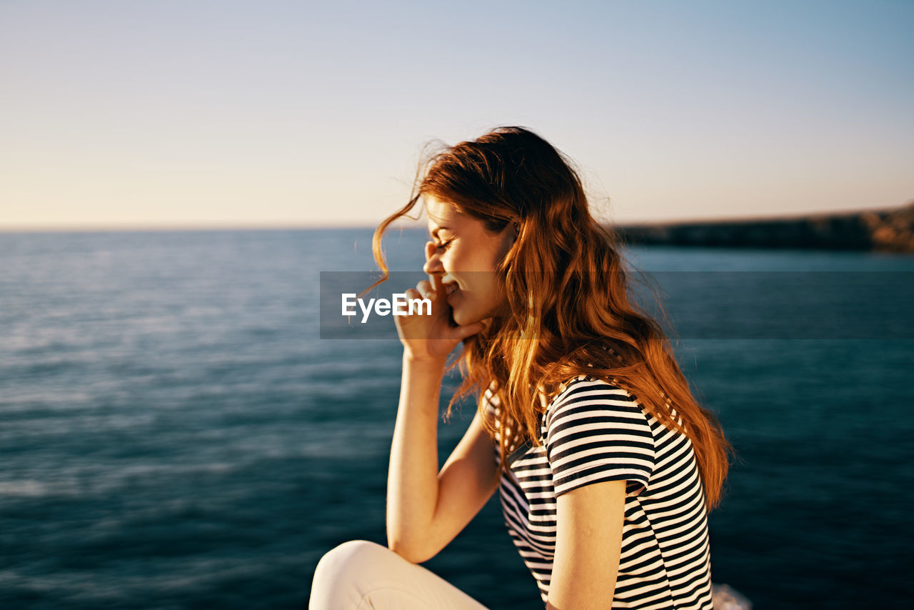 WOMAN SITTING IN SEA AGAINST SKY