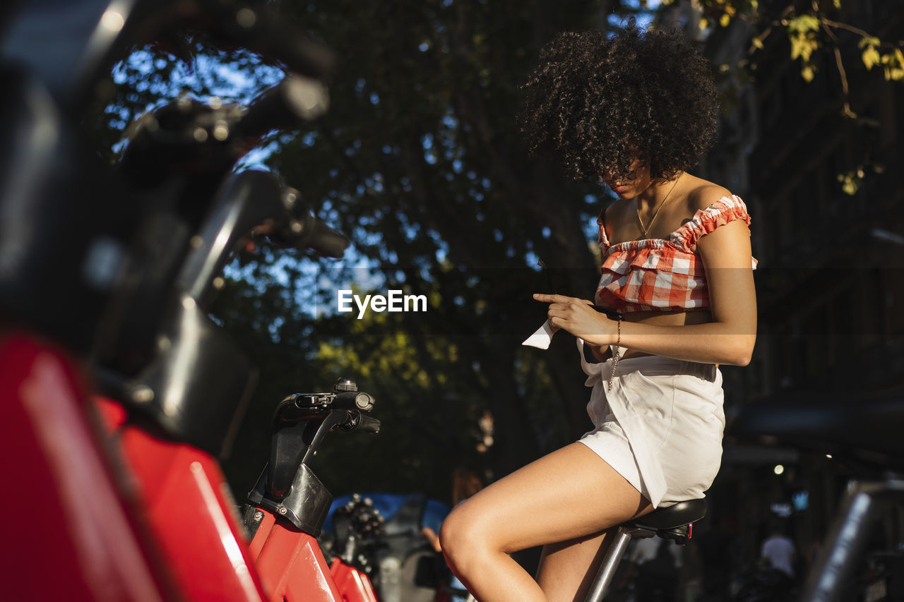 Curly hair woman using smartphone to scan shared bicycle