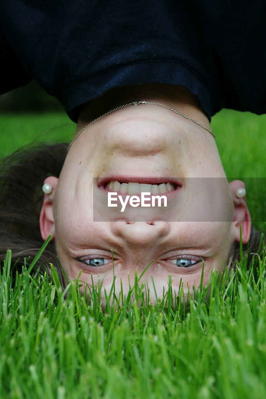 Portrait of smiling woman doing headstand on grass at park