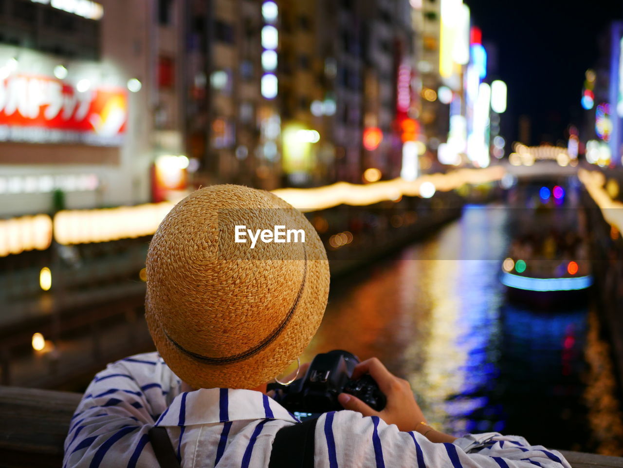 Rear view of woman photographing illuminated boat in city at night