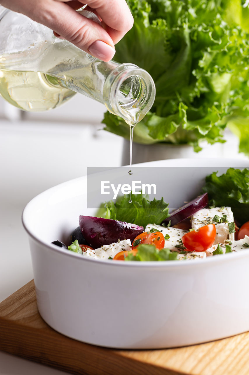 food and drink, food, vegetable, healthy eating, hand, salad, wellbeing, one person, produce, dish, freshness, adult, fruit, lettuce, bowl, indoors, green, pouring, holding, tomato, meal, lifestyles, herb, organic, ingredient, salad bowl, greek salad, domestic room