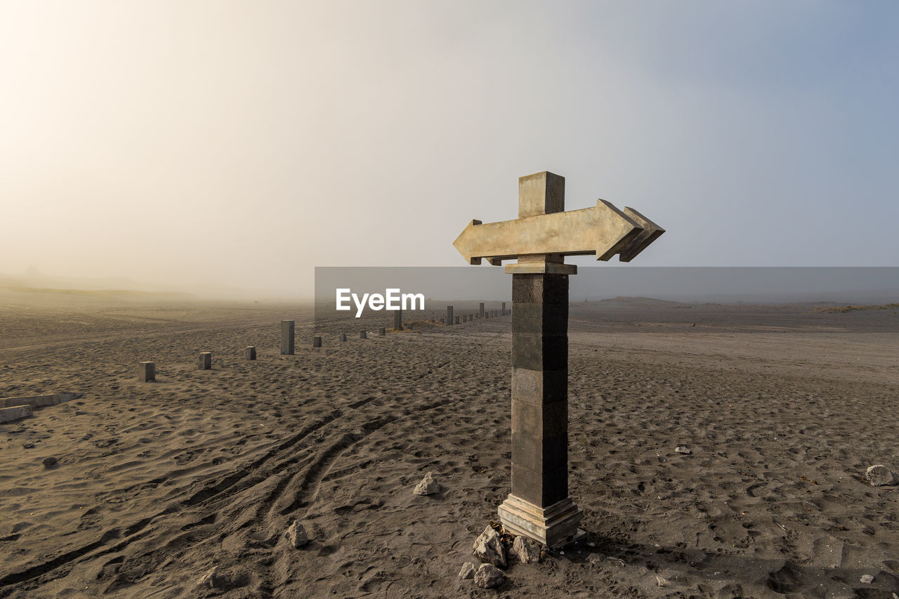 Stone sign post with opposite arrows and copy space in dry landscape and dirt road, java, indonesia