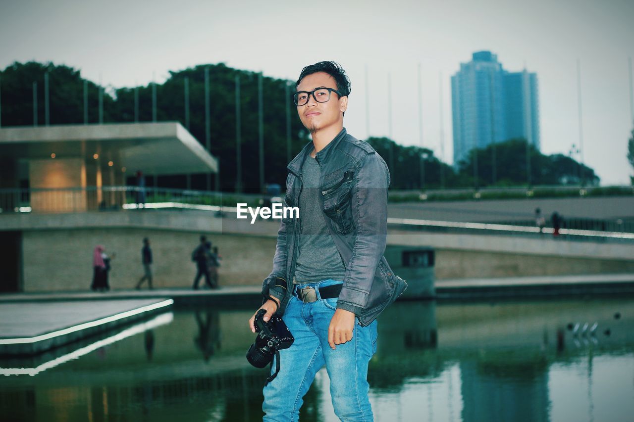 Portrait of man standing against pond in city