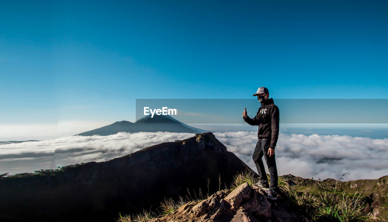Man gesturing thumbs up while standing on mountain against sky