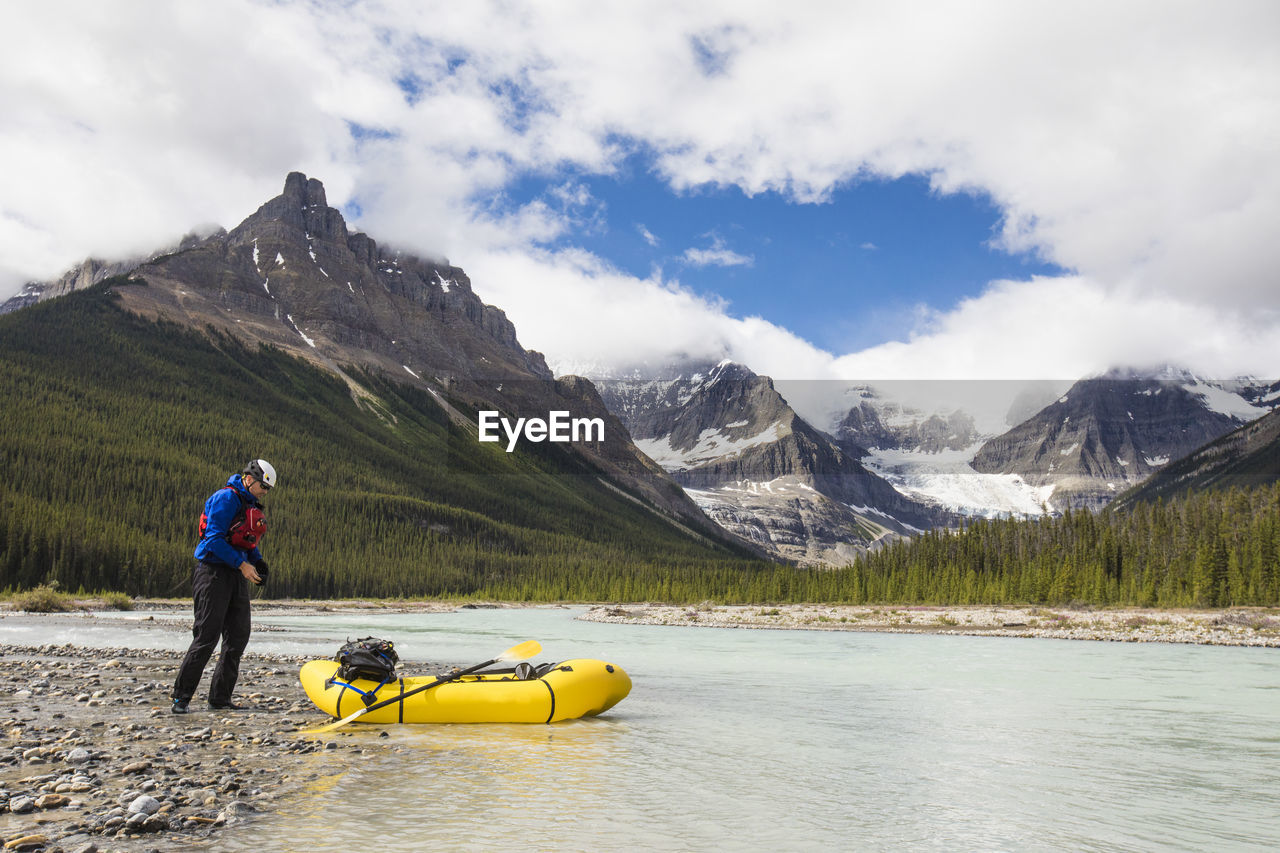Man exploring the rocky mountains in a packraft stops for a break.