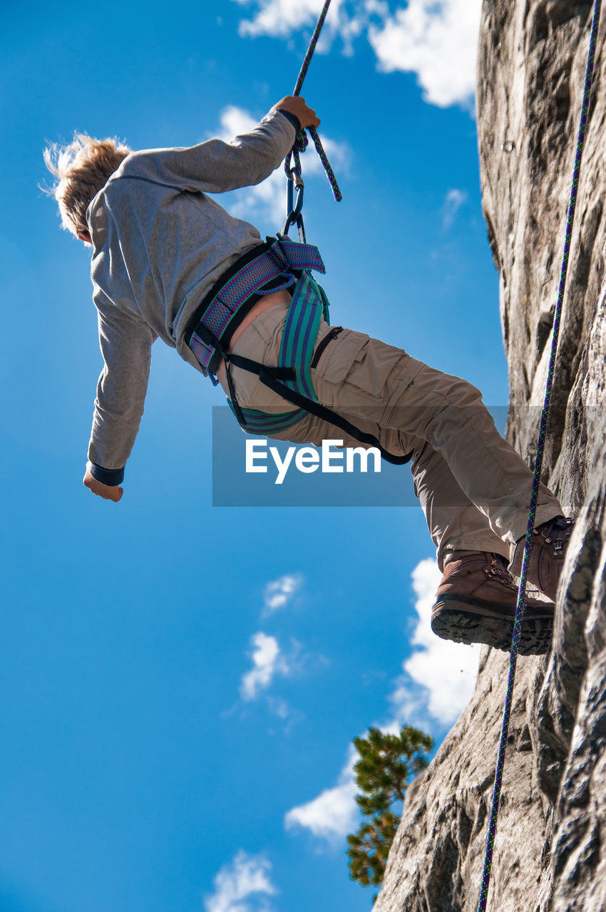 Low angle view of girl climbing on rock against sky