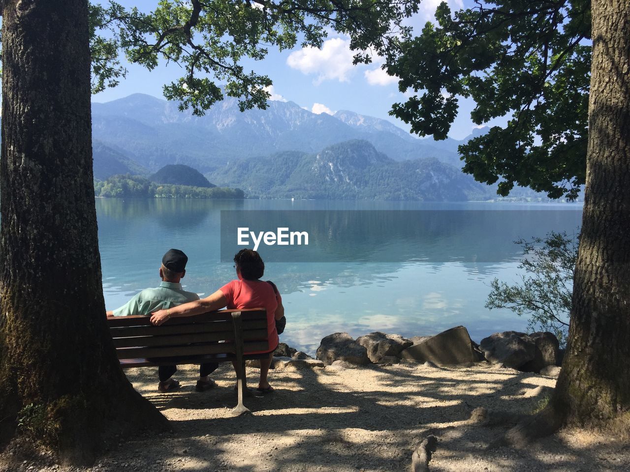 Rear view of people looking at lake while sitting on bench