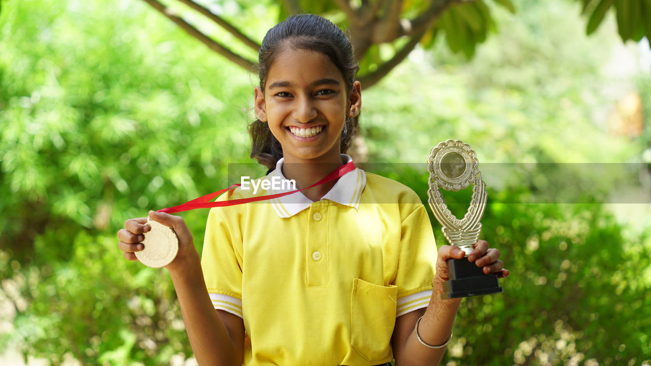 Portrait of a happy school girl wearing school uniform celebrating victory trophy in hand.