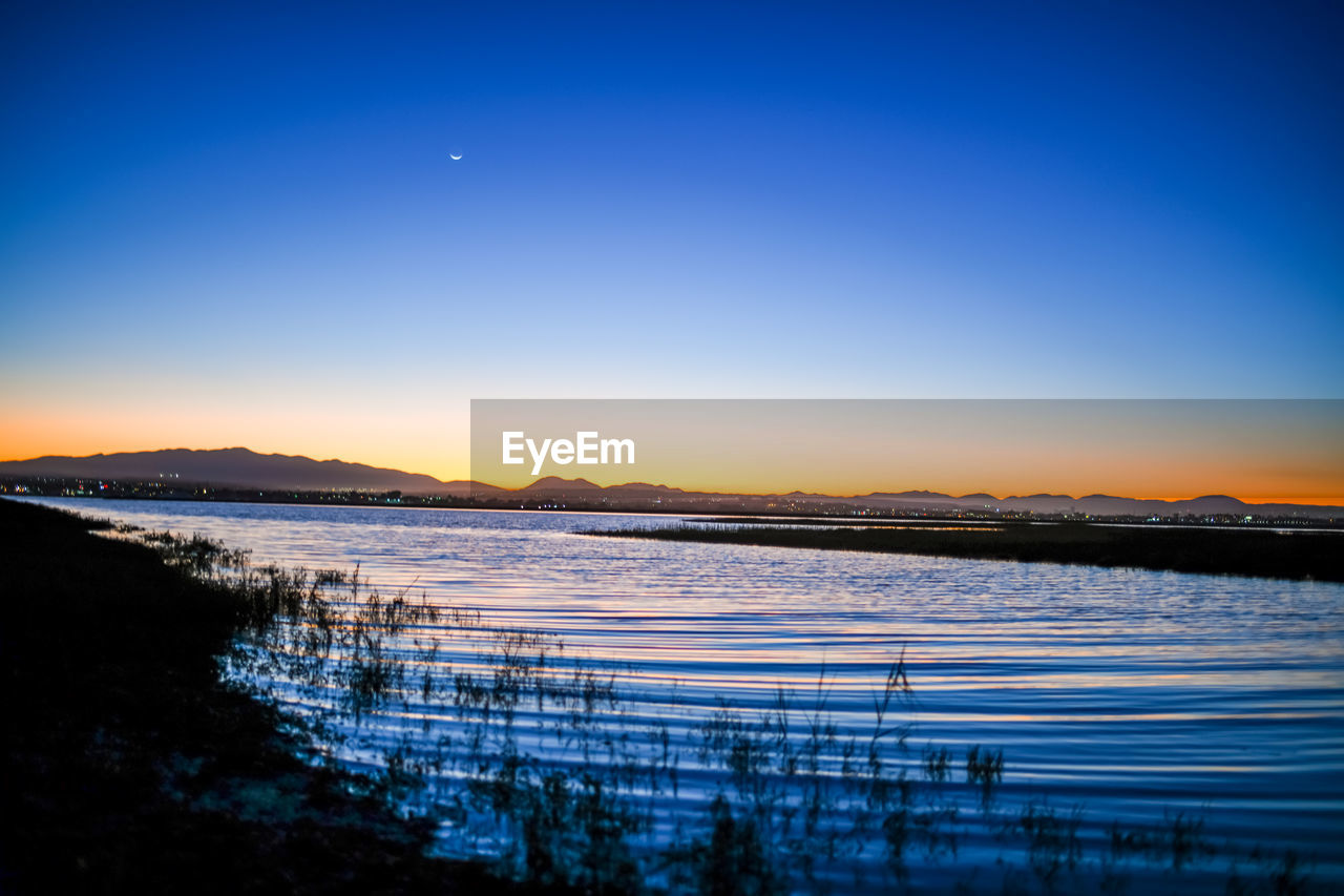 SCENIC VIEW OF LAKE AGAINST CLEAR BLUE SKY AT SUNSET