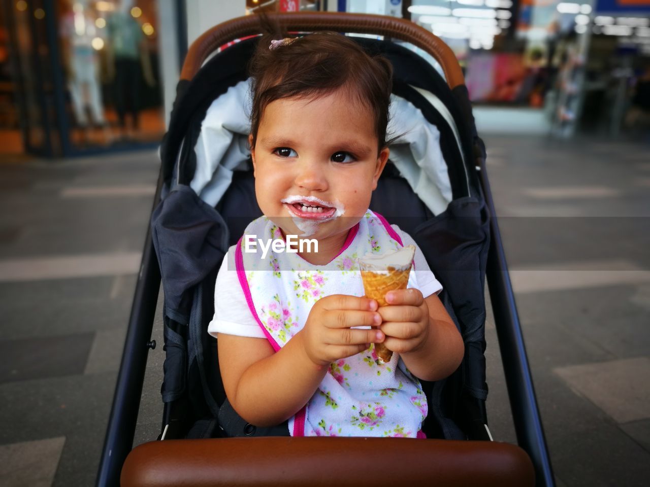 Cute girl eating ice cream while sitting in baby carriage